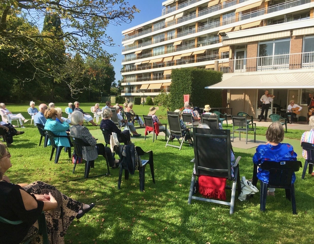 We zien een groep ouderen genieten van een live optreden. Het optreden bestaat uit een viool, een basist, een gitaarspeler en meer.